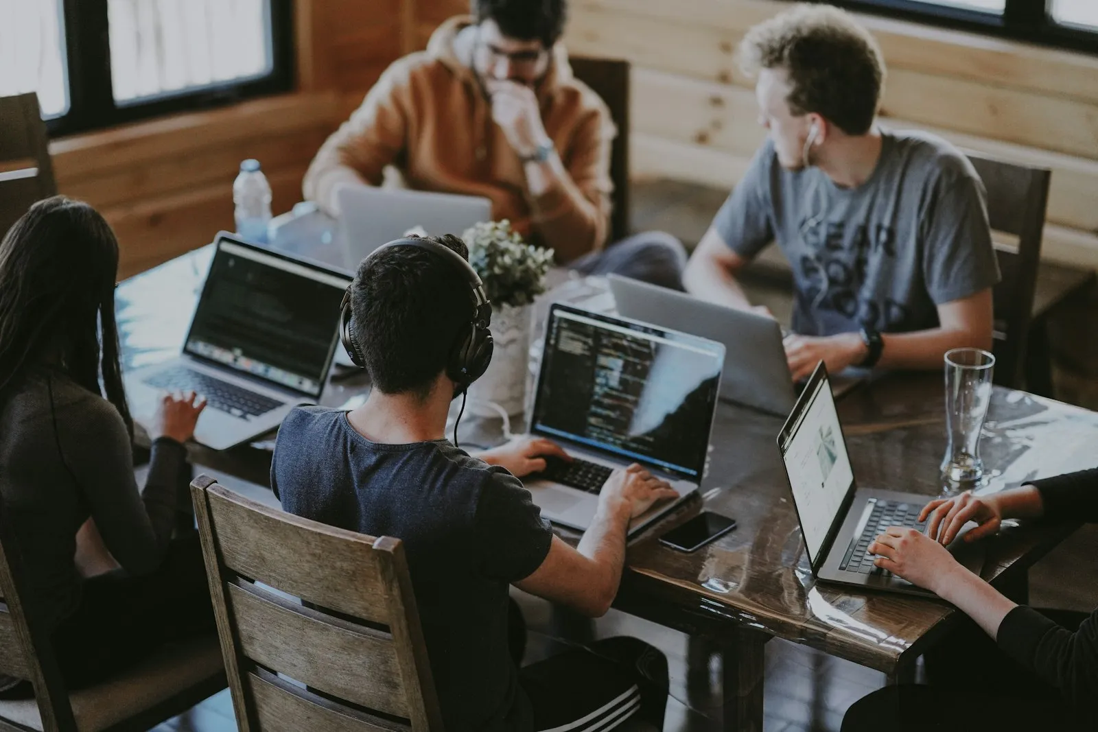 Profissionais colaborando em volta de uma mesa, com laptops e código na tela